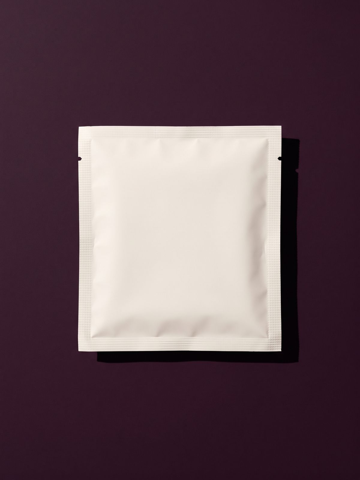 A plain white sachet lying flat on a plum surface.