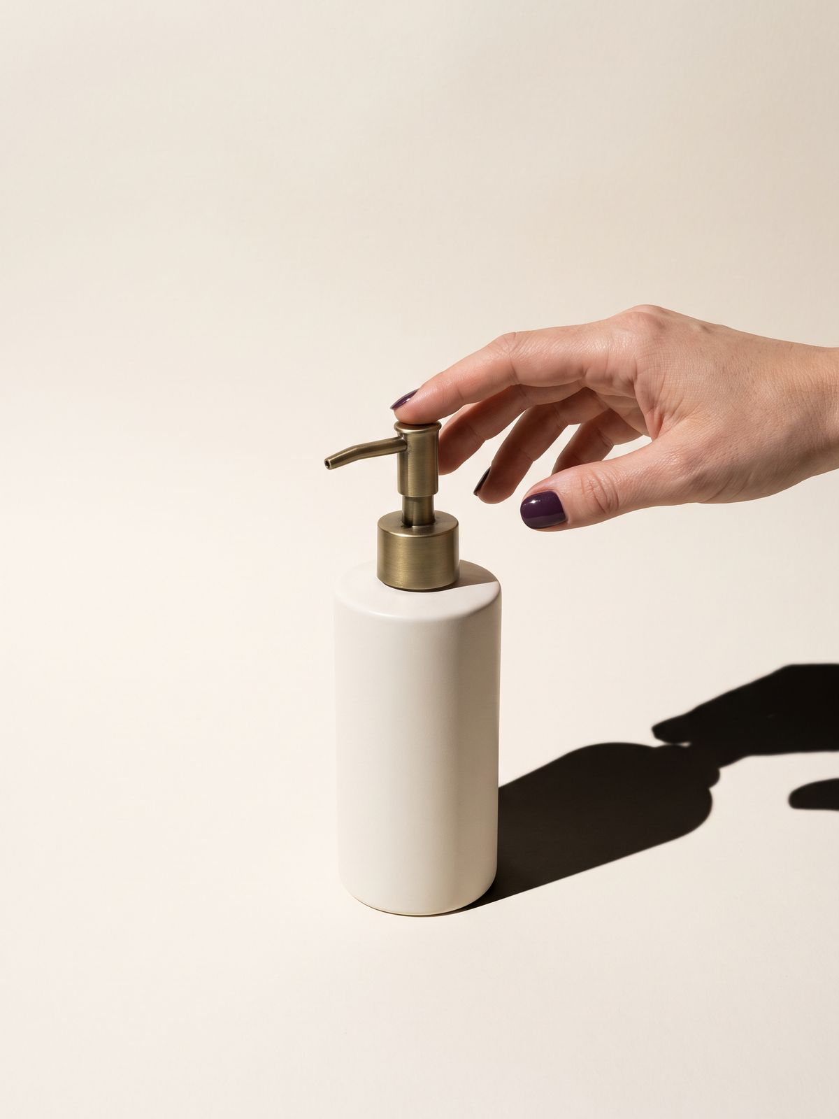 A white bottle with a brass pump and a hand reaching toward it.