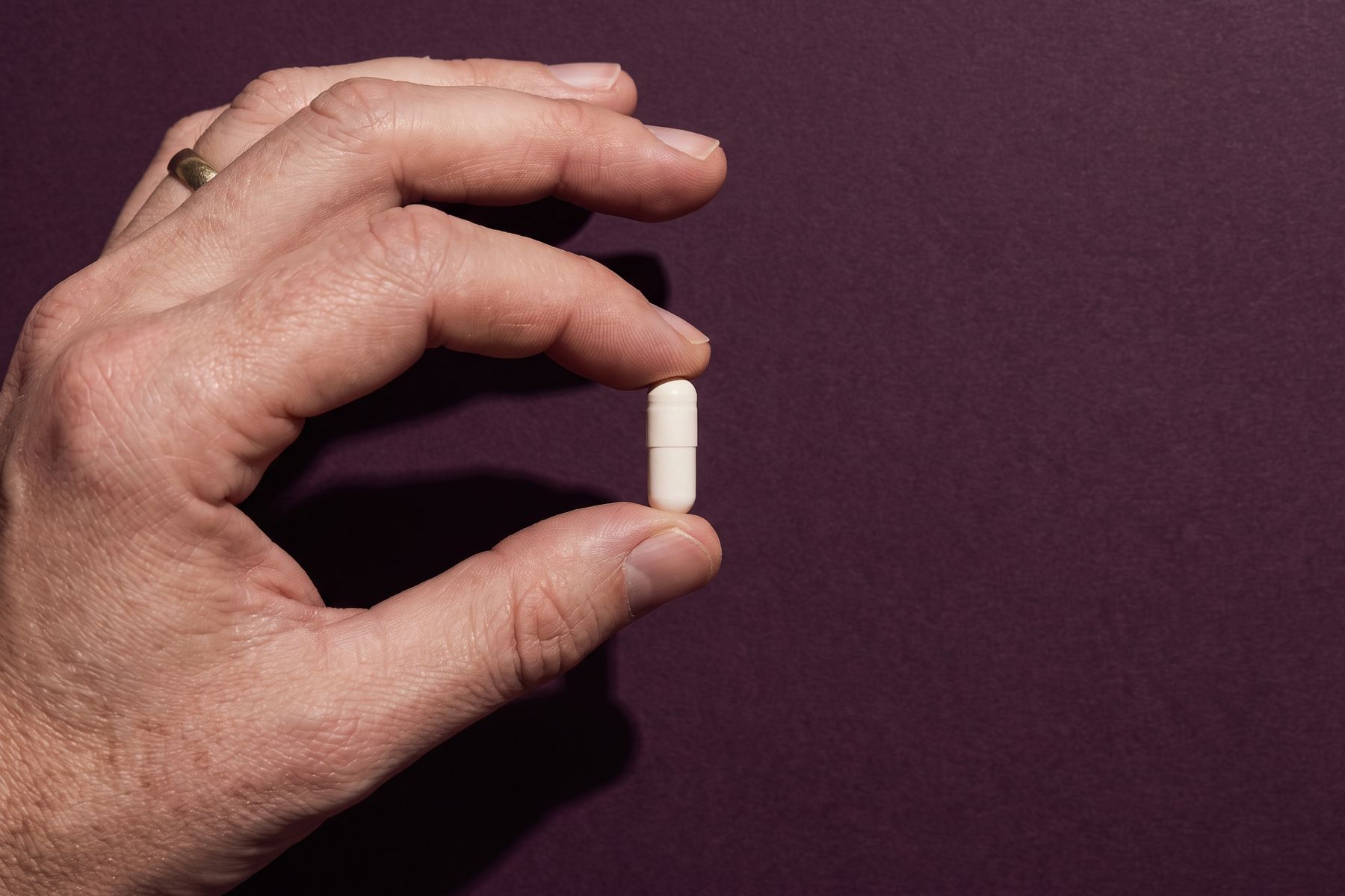 A hand holding a single plain capsule under one hard light.