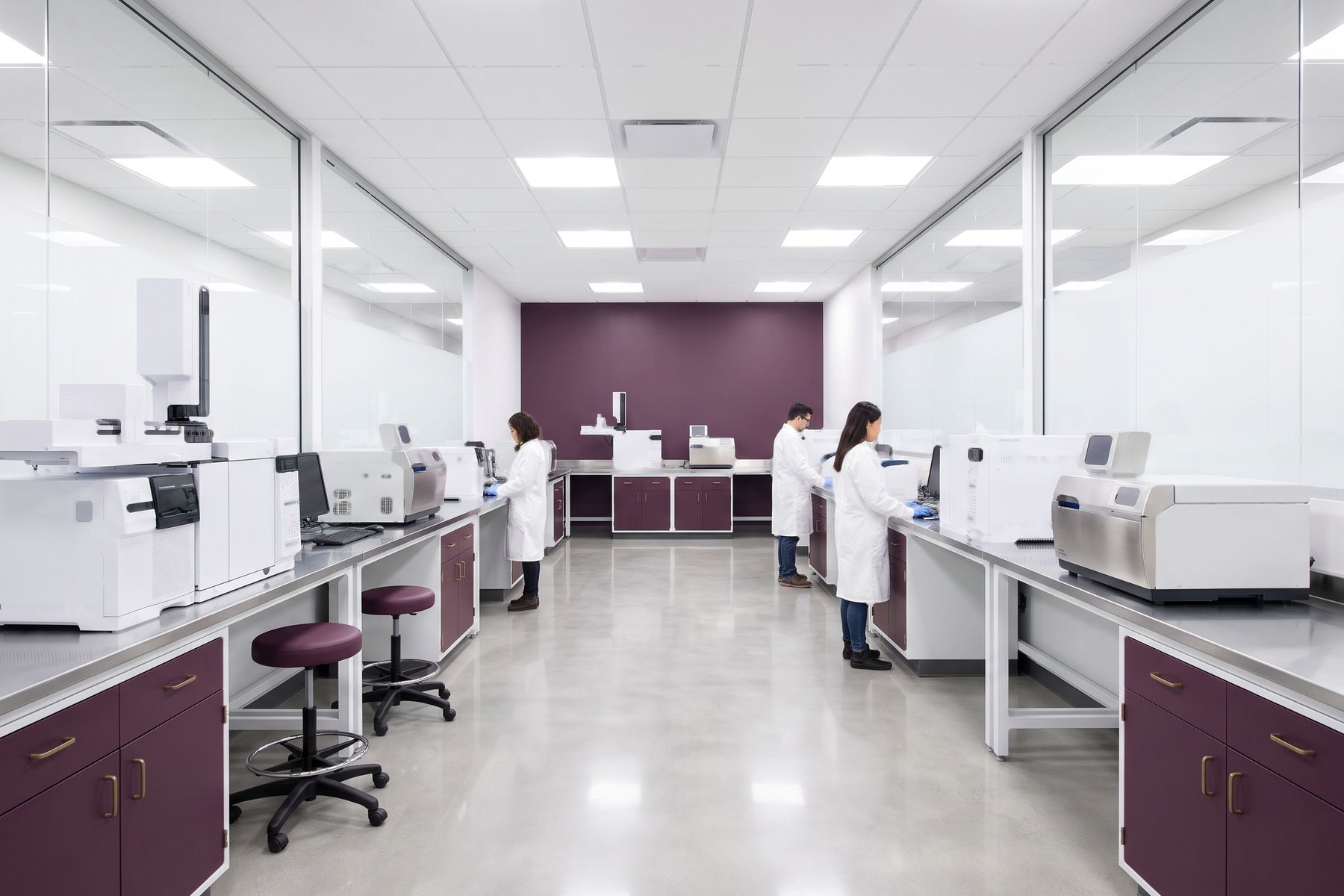 A bright laboratory with instruments along both benches and staff in white coats at work.