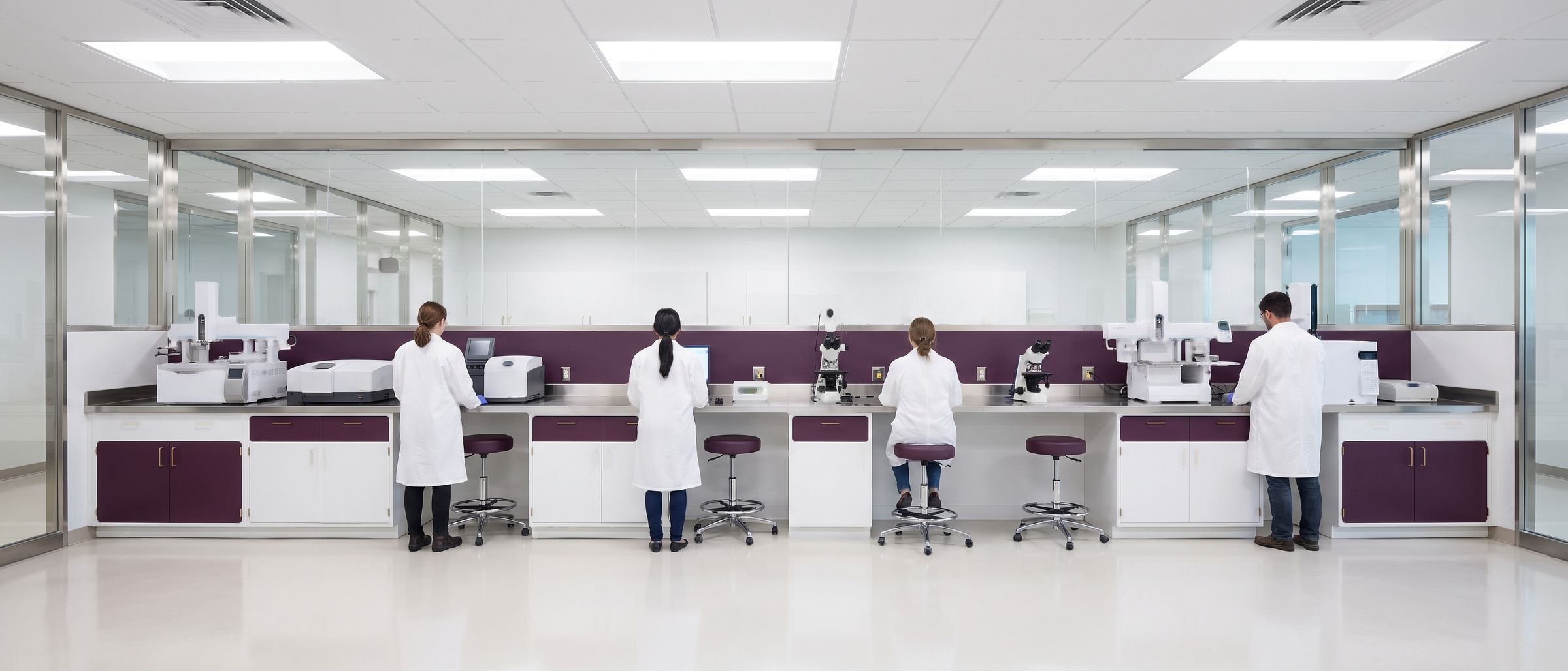 A long laboratory bench with four people in white coats working at separate stations.