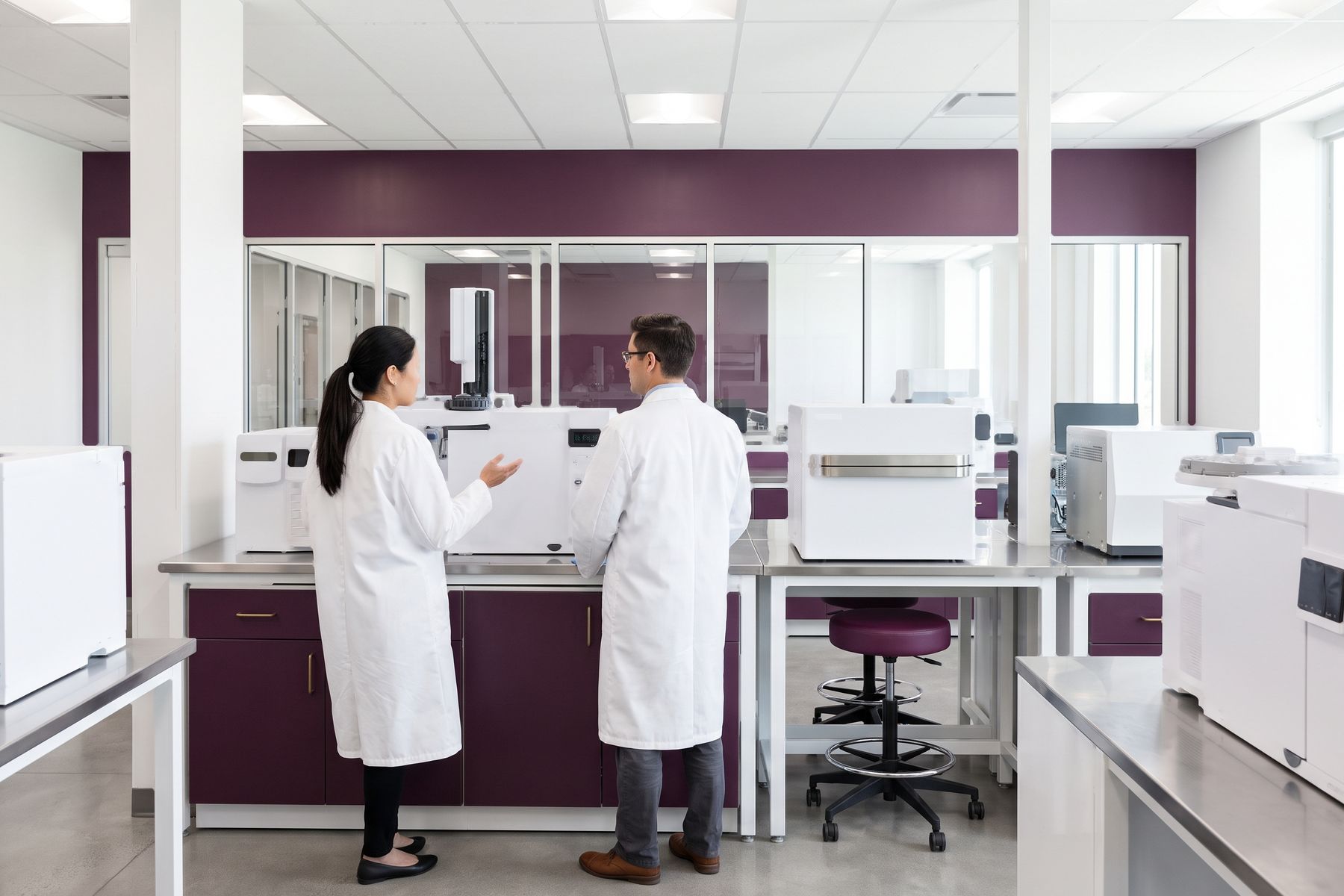 Two people in white laboratory coats discussing an instrument at a bench.